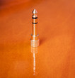 Golden headphone jack plug on a reflective wooden background.