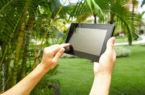 Photo: Hands with tablet computer in tropical garden. Hands with tablet computer in tropical garden.