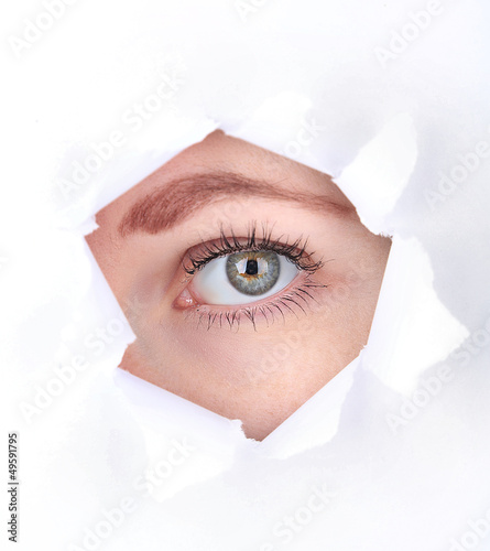 Photo: Female eye looking through hole in sheet of paper Female eye looking through hole in sheet of paper