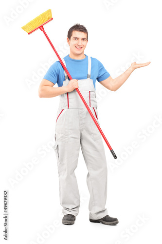 Photo: Full length portrait of a cleaner in a uniform with a broom poin Full length portrait of a cleaner in a uniform with a broom poin