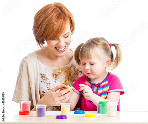 Photo: Happy child girl and mother sitting at table and playing with co Happy child girl and mother sitting at table and playing with co
