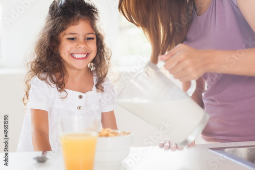 Photo: Mother putting milk in the cereal of his daughter Mother putting milk in the cereal of his daughter