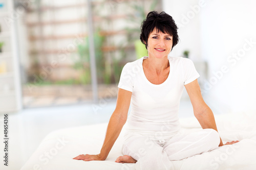 Photo: happy middle aged woman sitting on bed at home happy middle aged woman sitting on bed at home