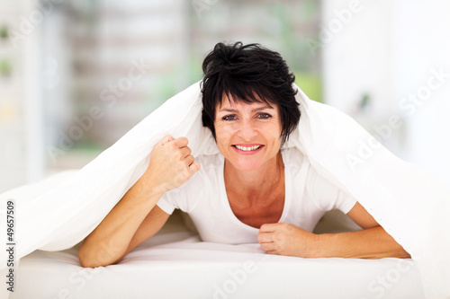 Photo: fun middle aged woman lying under duvet on bed fun middle aged woman lying under duvet on bed