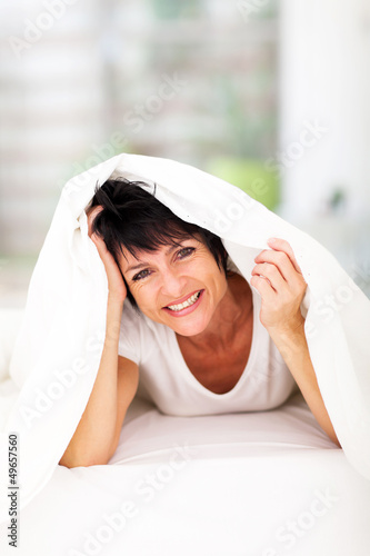 Photo: fun middle aged woman lying under duvet laughing fun middle aged woman lying under duvet laughing