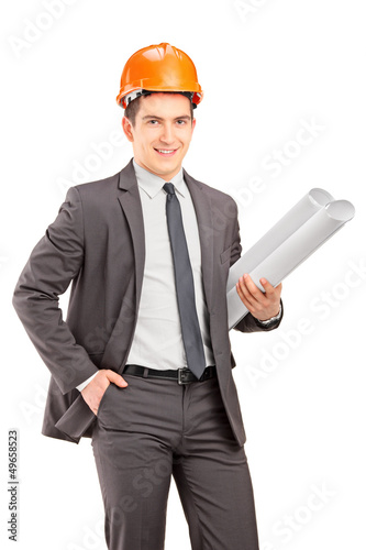 Photo: Young male engineer with helmet holding blueprints Young male engineer with helmet holding blueprints