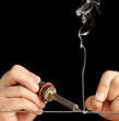 Soldering Tech soldering a gray wire on a pure black background.