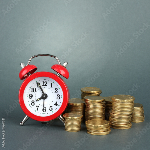 Photo: Alarm clock with coins on grey background Alarm clock with coins on grey background