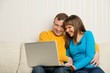 Photo: Smiling man and woman with laptop sitting on sofa Smiling man and woman with laptop sitting on sofa