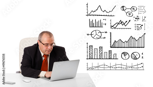 Photo: Businessman sitting at desk with diagrams and laptop Businessman sitting at desk with diagrams and laptop