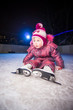 Photo: Adorable girl in skates sit on ice rink after fall in evening Adorable girl in skates sit on ice rink after fall in evening