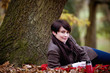 A woman sitting under a tree holding a hot drink in autumn