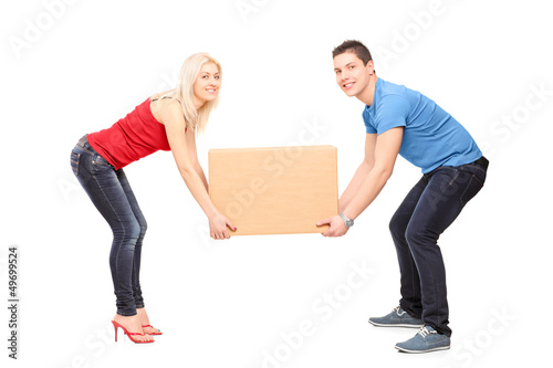 Photo: Full length portrait of a young couple trying to lift a box Full length portrait of a young couple trying to lift a box