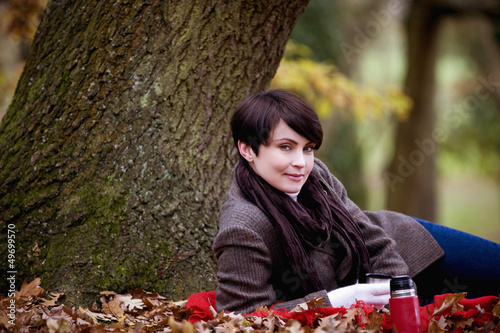 Photo: A woman sitting under a tree holding a hot drink in autumn A woman sitting under a tree holding a hot drink in autumn