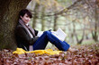 A woman sitting under a tree in autumn time, holding a book