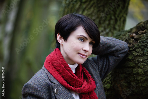 Photo: A woman leaning against a tree in autumn time A woman leaning against a tree in autumn time