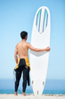 Photo: Rearview of young surfer in his wetsuit holding his surfboard wh Rearview of young surfer in his wetsuit holding his surfboard wh