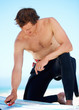 A young surfer scraping wax of his surfboard with his card