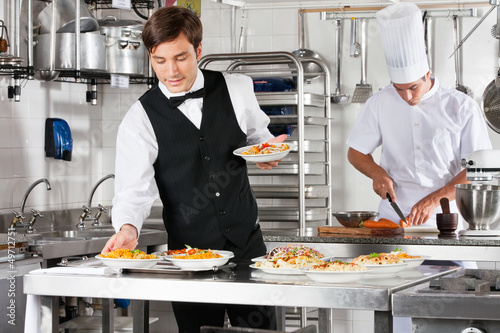 Photo: Waiter And Chef Working In Commercial Kitchen Waiter And Chef Working In Commercial Kitchen
