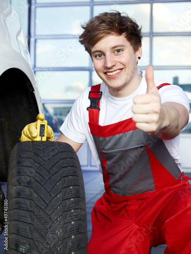 Photo: Mechanic checks the tread pattern of a winter tire, shows thumb Mechanic checks the tread pattern of a winter tire, shows thumb