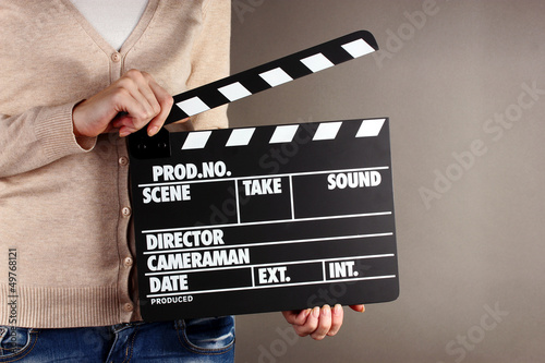 Photo: Movie production clapper board in hands on grey background Movie production clapper board in hands on grey background