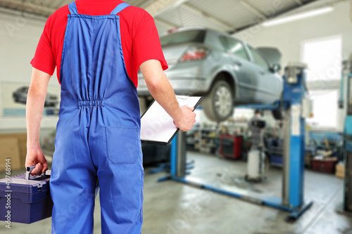 Photo: Mechanic with a tool box and clipboard standing in a repair serv Mechanic with a tool box and clipboard standing in a repair serv