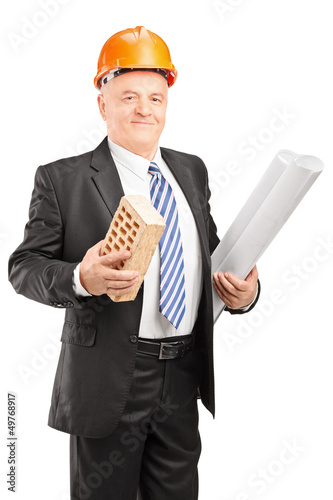Photo: Portrait of a smiling mature architect holding a brick and bluep Portrait of a smiling mature architect holding a brick and bluep