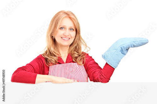 Photo: Smiling woman in apron posing with a cooking mitten behind a pan Smiling woman in apron posing with a cooking mitten behind a pan