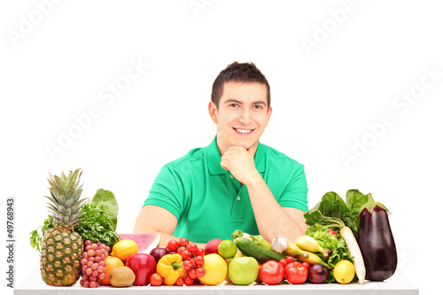 Photo: Young man posing with a pile of fruits and vegetables Young man posing with a pile of fruits and vegetables