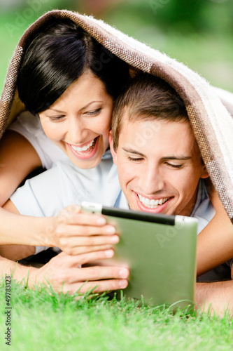 Photo: Happy couple lying on the green grass with pad Happy couple lying on the green grass with pad