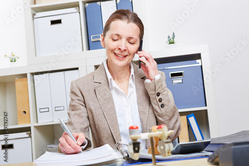Photo: Frau im Büro telefoniert mit Smartphone Frau im Büro telefoniert mit Smartphone