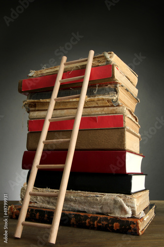 Photo: Old books and wooden ladder, on grey background Old books and wooden ladder, on grey background