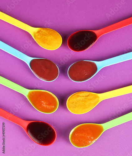 Photo: Baby puree in spoons on purple background Baby puree in spoons on purple background