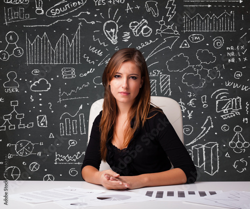 Photo: Businesswoman sitting at desk with business scheme and icons Businesswoman sitting at desk with business scheme and icons