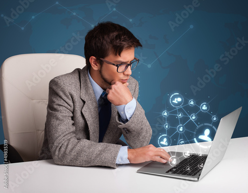 Photo: Young man sitting at desk and typing on laptop with social netwo Young man sitting at desk and typing on laptop with social netwo