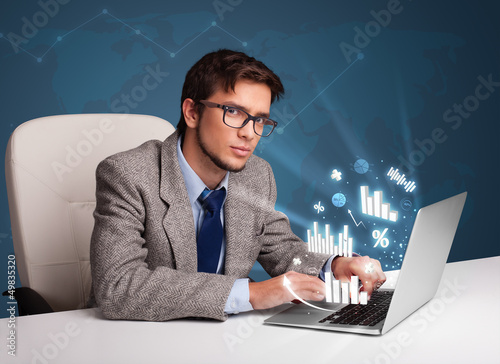 Photo: Young man sitting at desk and typing on laptop with diagrams and Young man sitting at desk and typing on laptop with diagrams and