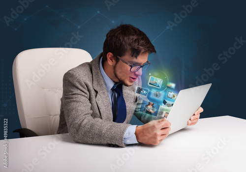 Photo: Young man sitting at desk and watching his photo gallery on lapt Young man sitting at desk and watching his photo gallery on lapt