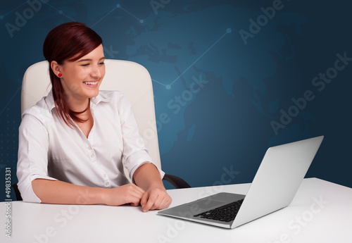 Photo: Young woman sitting at desk and typing on laptop Young woman sitting at desk and typing on laptop