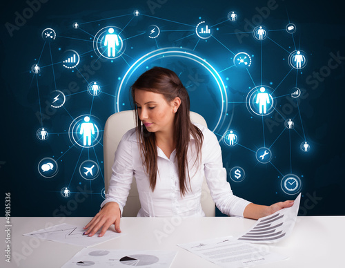 Photo: Businesswoman sitting at desk with social network icons Businesswoman sitting at desk with social network icons