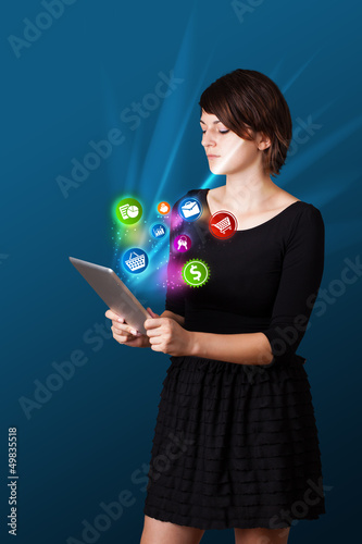 Photo: Young woman looking at modern tablet with abstract lights and va Young woman looking at modern tablet with abstract lights and va