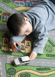 Small child boy playing on a road themed carpet with a toy car.