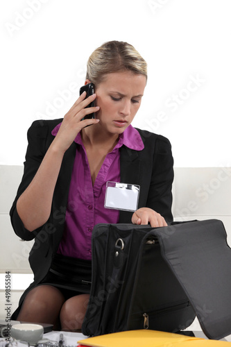Photo: Businesswoman looking through briefcase whilst on the phone Businesswoman looking through briefcase whilst on the phone