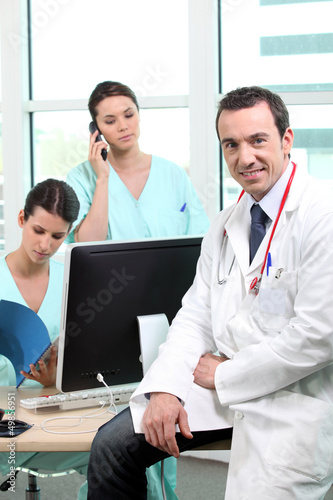 Photo: Doctor sitting with nurses at a computer Doctor sitting with nurses at a computer