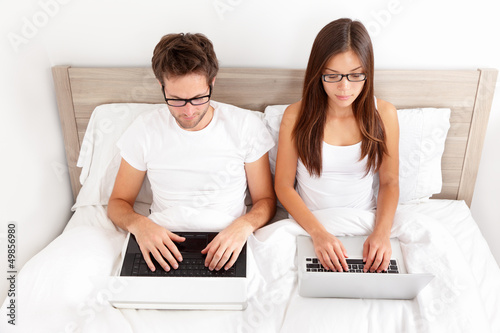 Photo: Couple working on laptops in bed Couple working on laptops in bed