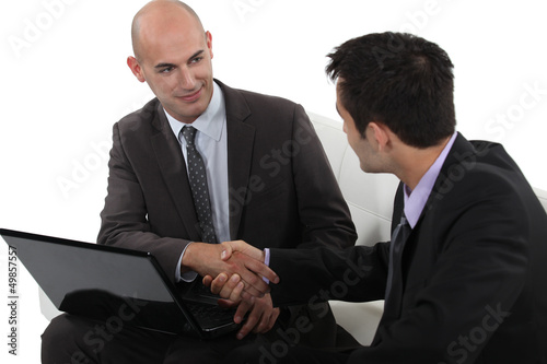 Photo: Businessmen shaking hands over a laptop Businessmen shaking hands over a laptop