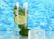 Glass of water with ice, mint and lime on sea background