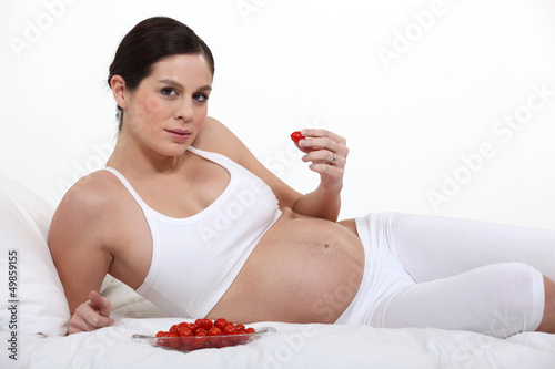 Photo: A pregnant woman eating strawberries in bed. A pregnant woman eating strawberries in bed.
