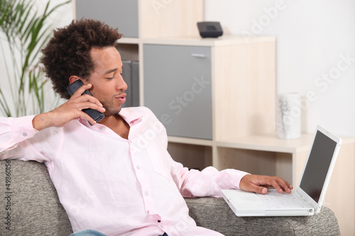 Photo: Couple sitting on sofa with computer and phone Couple sitting on sofa with computer and phone