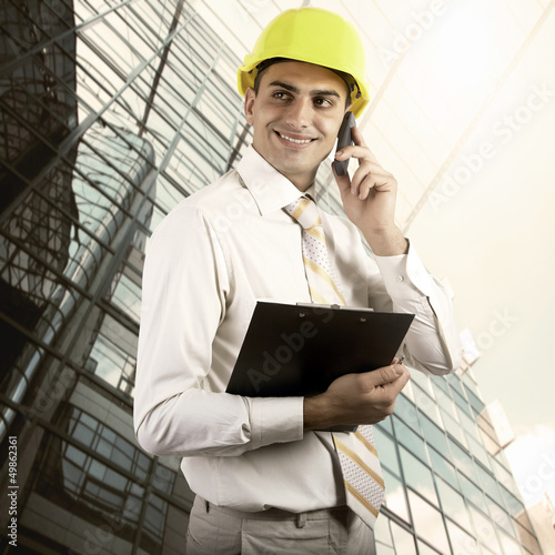 Photo: Young architect wearing a protective helmet standing on the buil Young architect wearing a protective helmet standing on the buil
