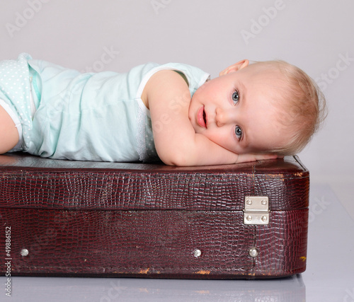 Photo: baby girl playing with suitcase on grey background baby girl playing with suitcase on grey background